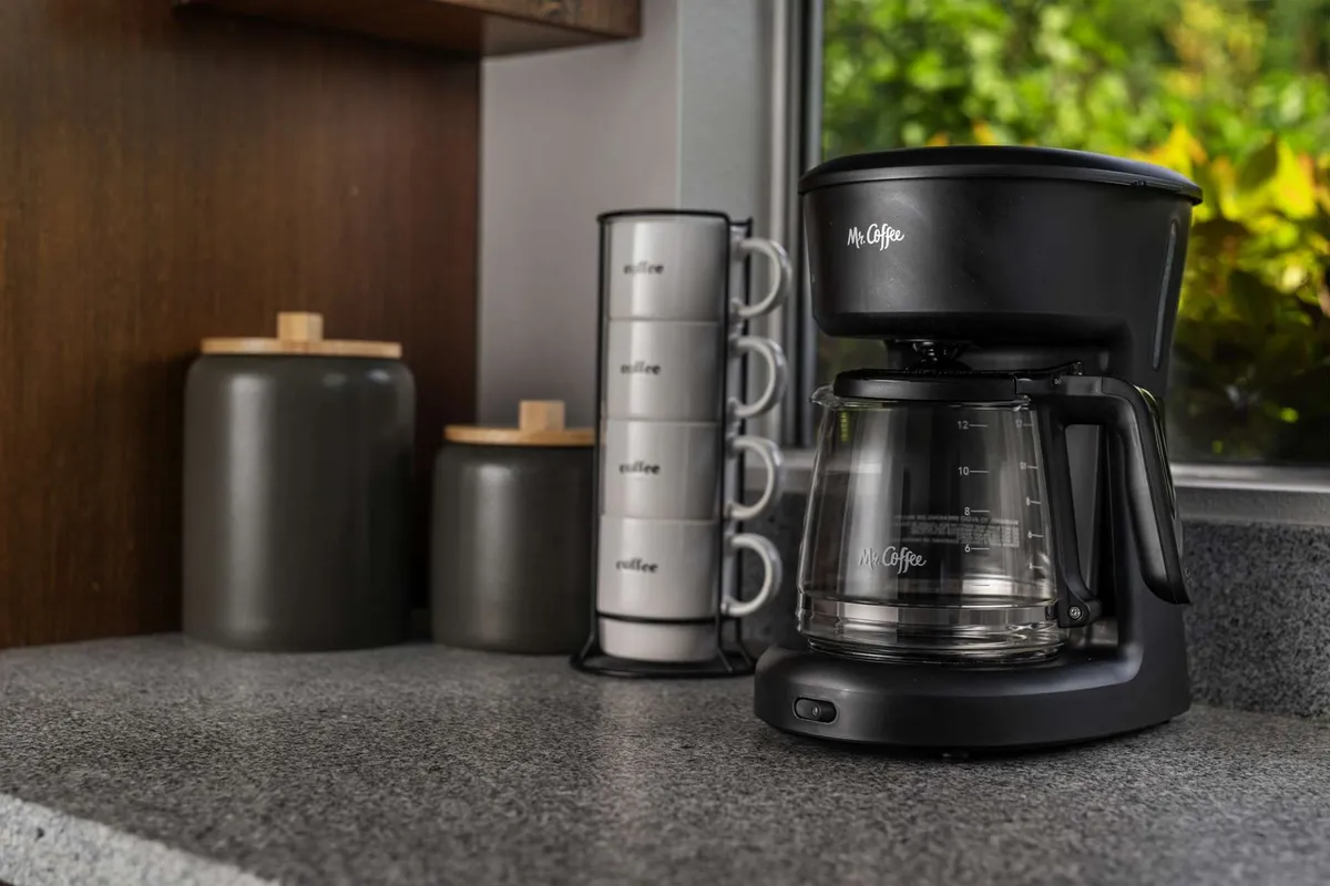 A cozy coffee station setup with a coffee maker, mugs, and storage jars, arranged on a countertop. The scene evokes the comfort of morning gatherings and casual snacks, reinforcing the kitchen's role as a welcoming hub for daily routines.