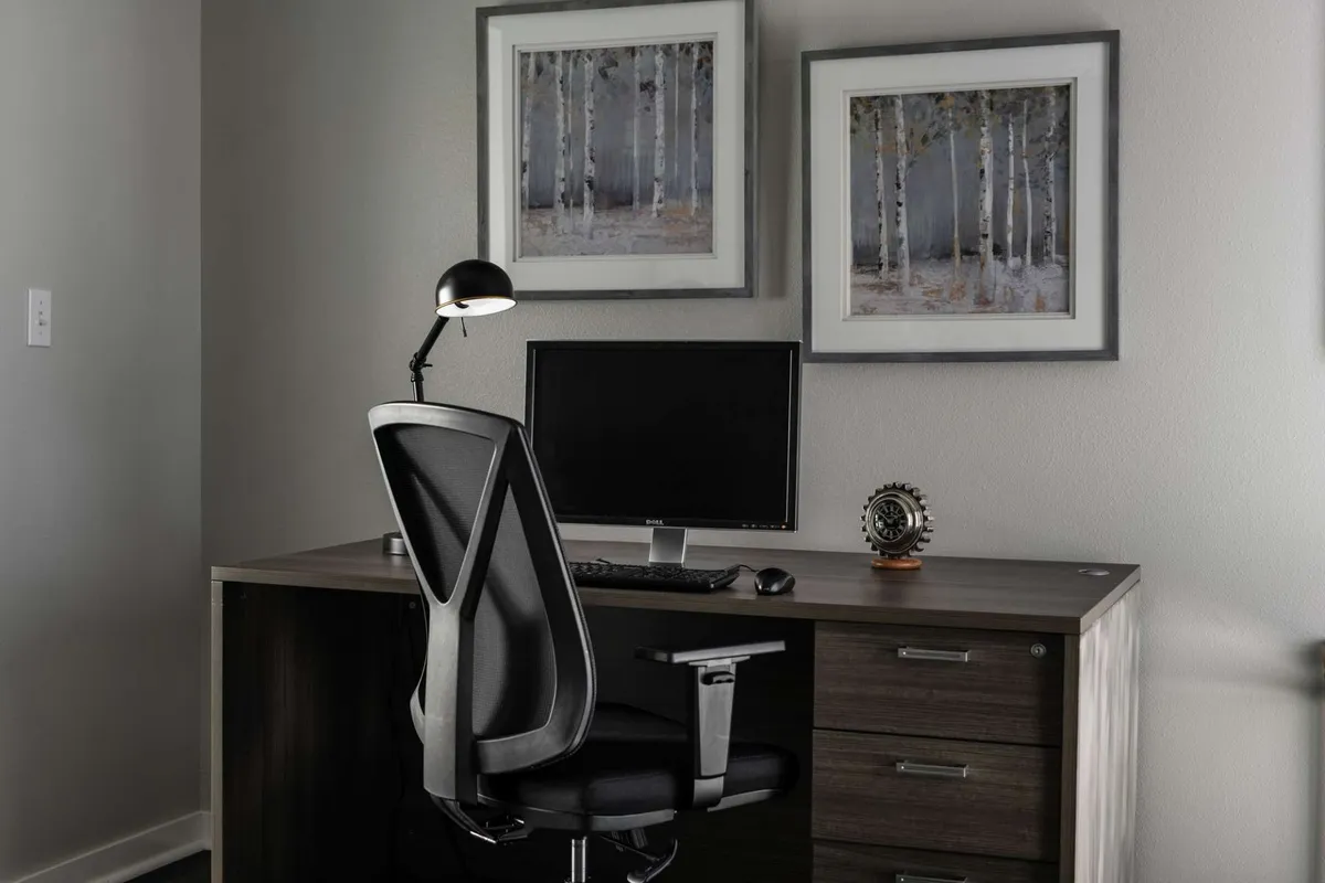 A thoughtfully arranged workspace is pictured with a modern desk, a computer monitor, tasteful wall art, and a warm lamp. The scene is set for focused work or study sessions, conveying an atmosphere conducive to productivity.