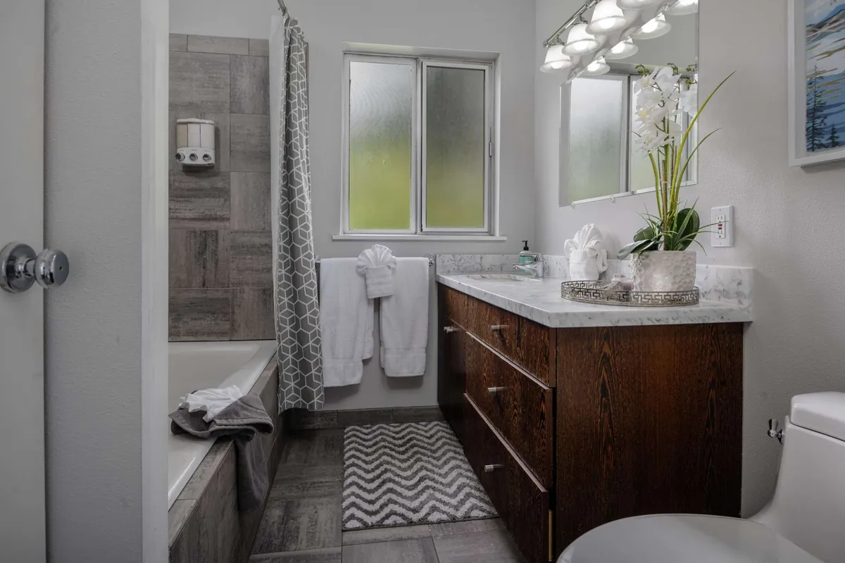 A bright, serene bathroom featuring a modern bathtub, vanity with a sink, a window bringing in natural light, and a decorative plant that adds a touch of tranquility. The clean, simple design emphasizes relaxation and refreshment.