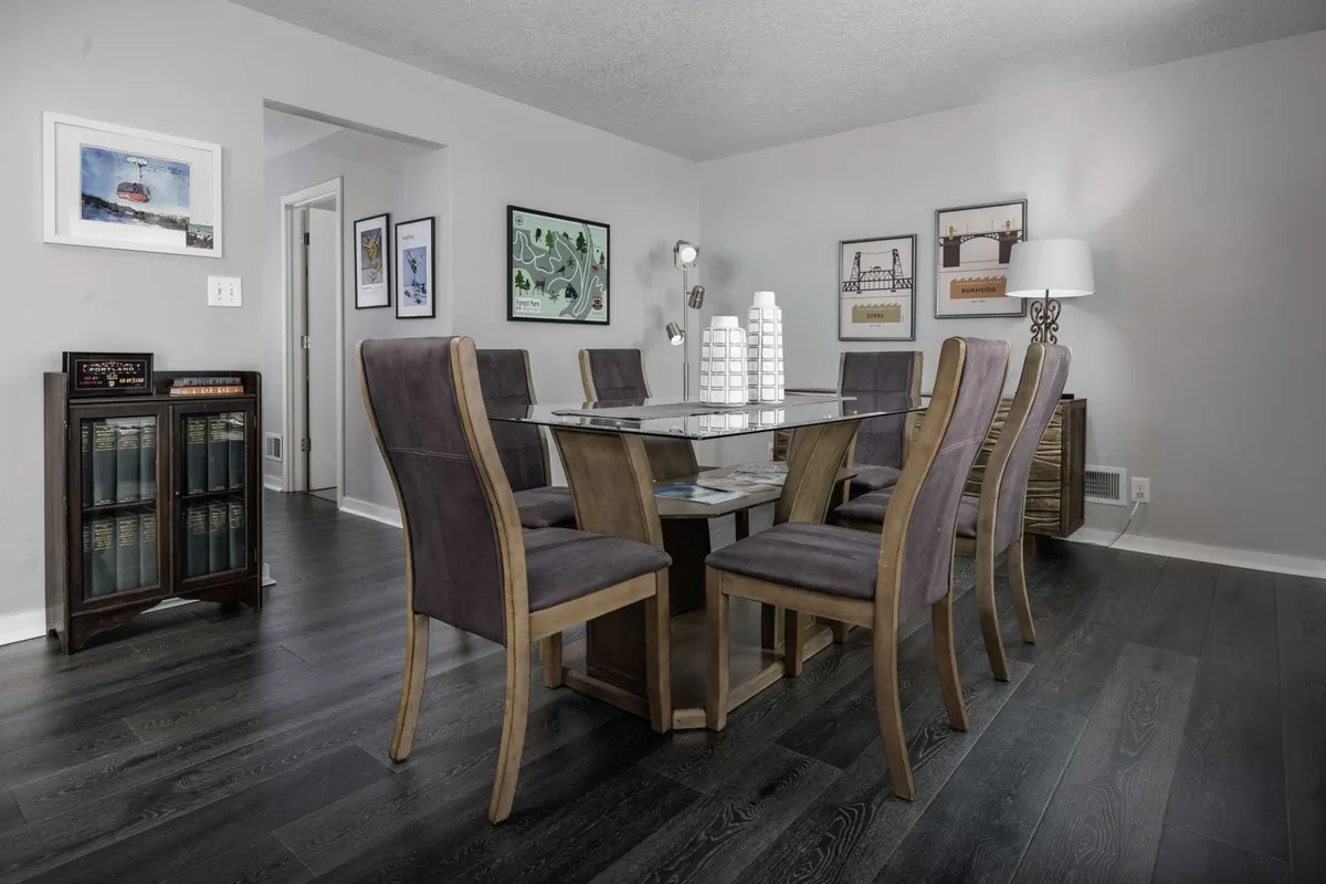 A welcoming dining area with a central table and chairs, artwork on the walls, and a side table with a lamp. The space is set up for group meals, celebrations, and shared moments, embodying the communal, family-friendly environment emphasized in the section.