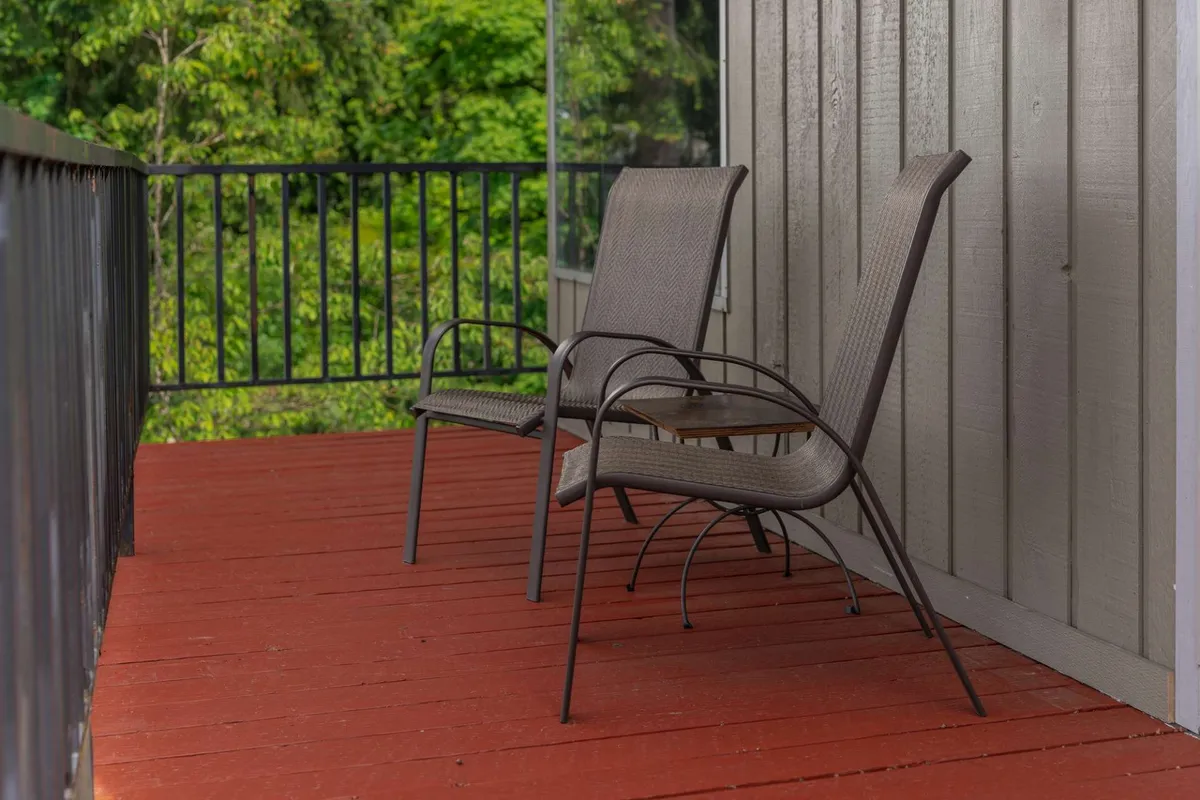 This image shows two comfortable chairs set on a wooden deck, surrounded by lush green foliage. The setup suggests a relaxing, secure outdoor space that's perfect for both people and pets to unwind while being safely contained.