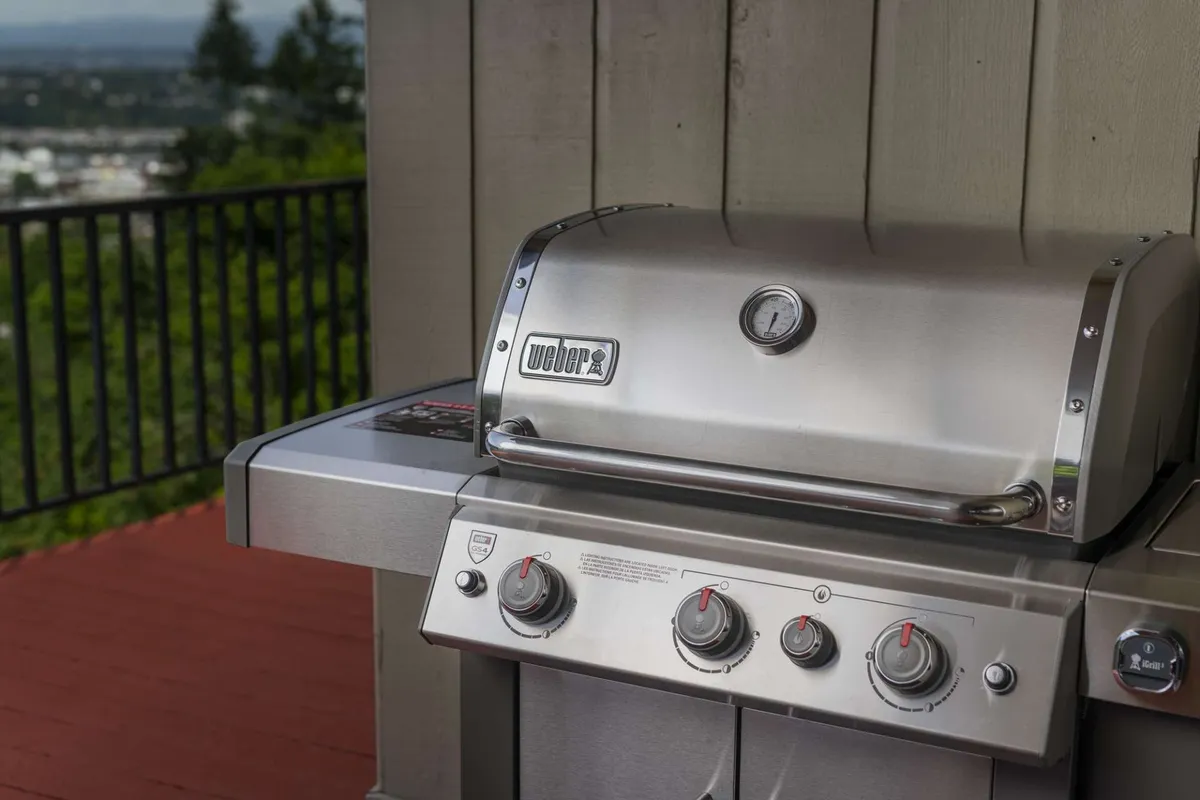 The image focuses on a stainless steel grill and wooden deck railing, suggesting a spacious deck suited for social gatherings, family meals, and outdoor relaxation. The setup implies ample room for both humans and pets to enjoy time together outside.